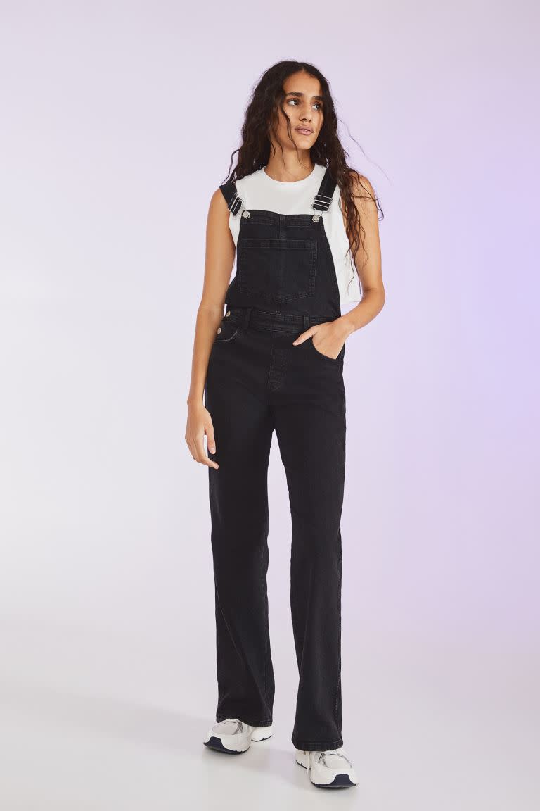 A woman stands in Flared Denim Dungarees