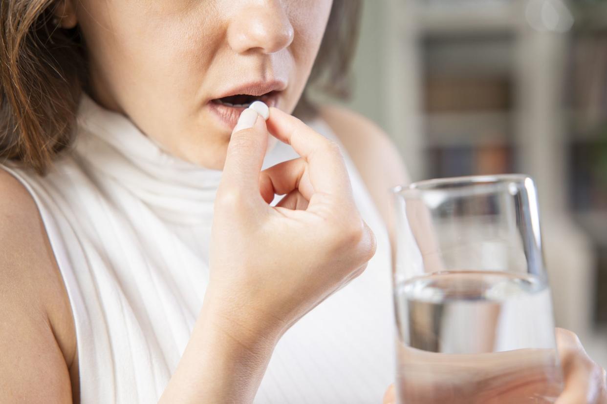 Cropped shot of young woman taking pill holding a glass of water sitting on a sofa at home