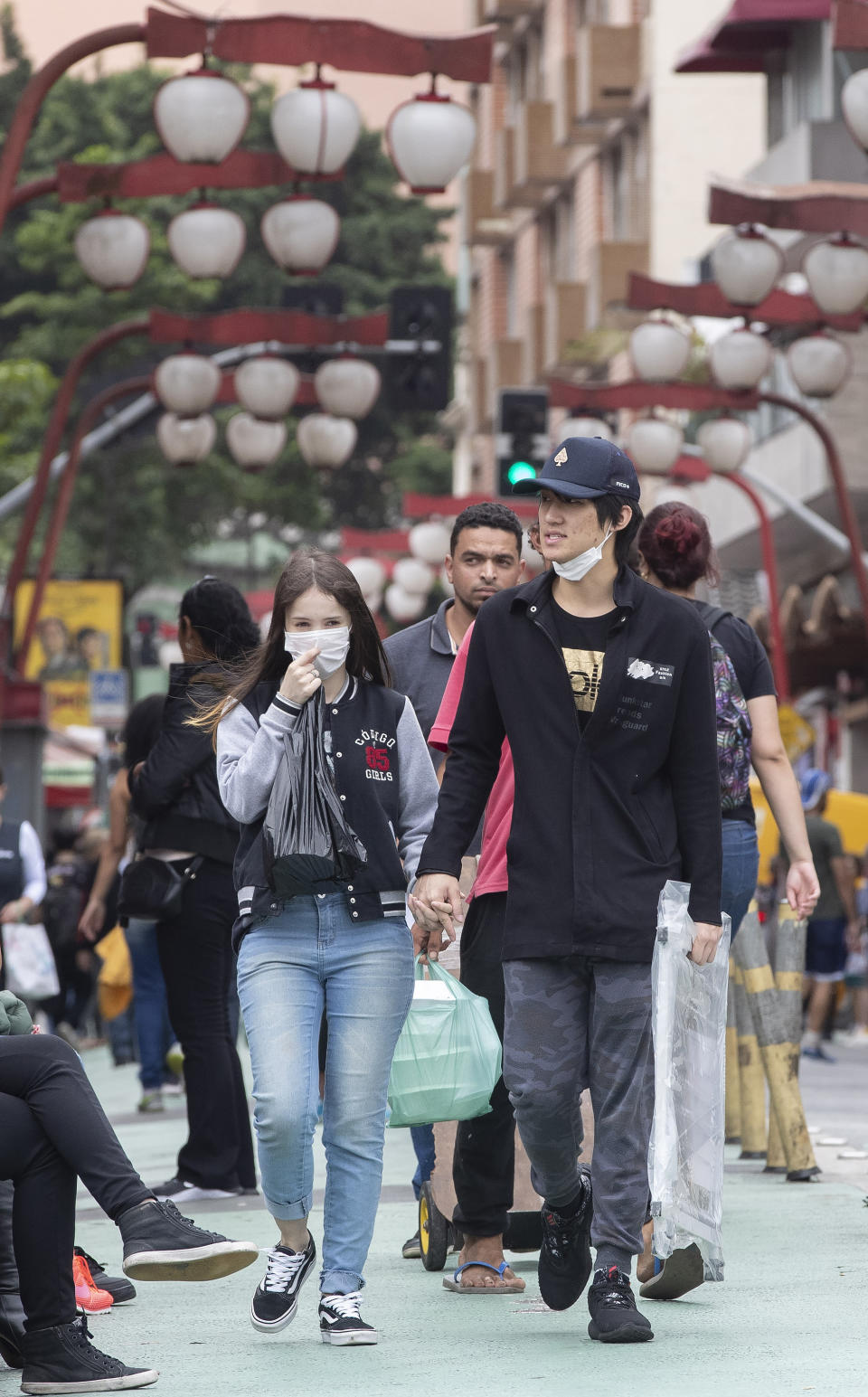 A couple wearing masks as a precaution against the spread of the new coronavirus COVID-19 walk in the Asian neighborhood of Liberdade in Sao Paulo, Brazil, Thursday, Feb. 27, 2020. (AP Photo/Andre Penner)