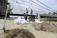 Workers clean oil spill along Sentosa's Palawan Beach area in Singapore, Sunday, June 16, 2024. An oil spill caused by a dredger boat hitting a stationary cargo tanker has blackened part of Singapore’s southern coastline, including the popular resort island of Sentosa, and sparked concerns it may threaten marine wildlife. (AP Photo/Suhaimi Abdullah)