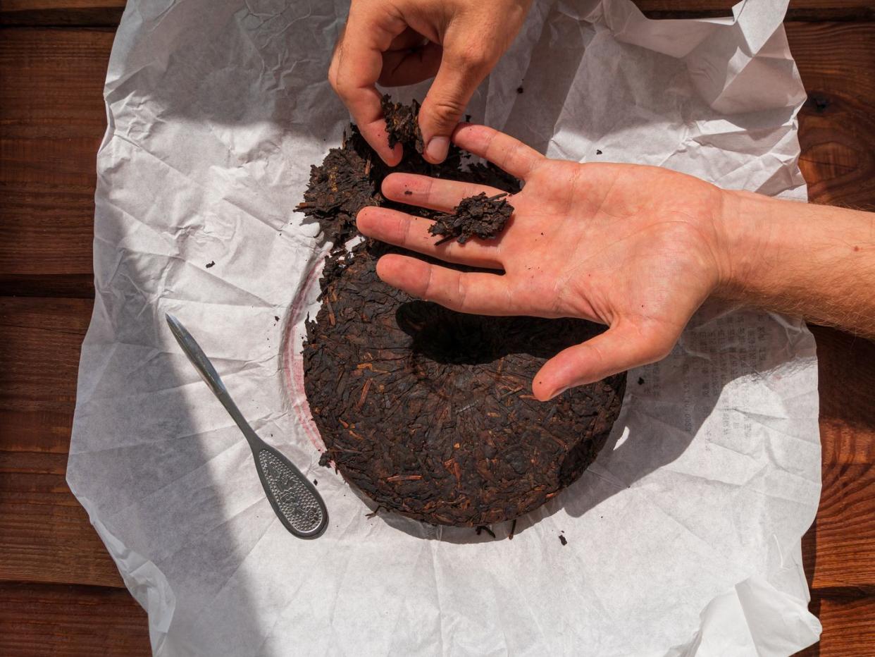 pressed round cake of fermented shu puerh tea on white paper with male hands holding a piece