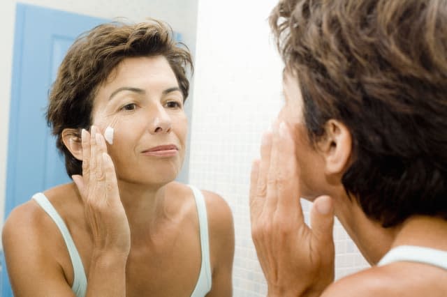 Woman applying face cream in front of mirror