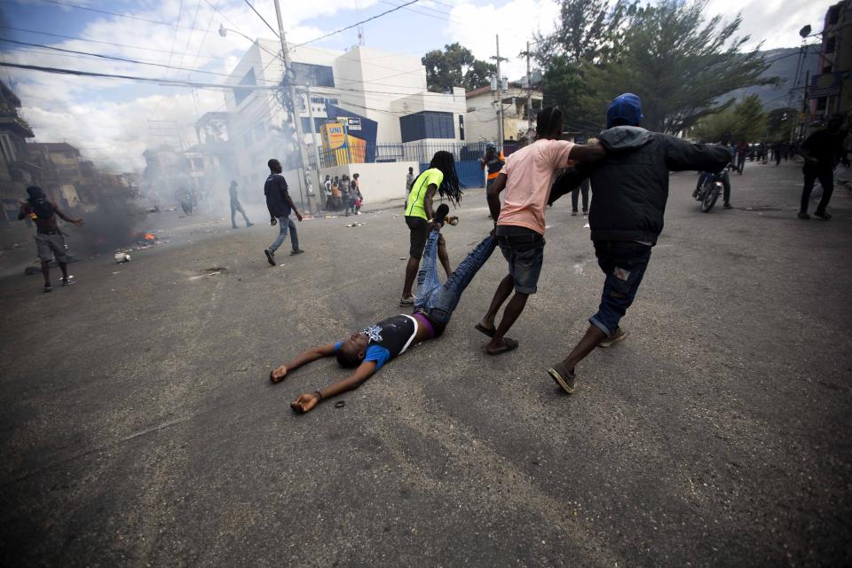 Demonstrators drag the body of a fellow protester toward police, as a form of protest after police shot into the crowd in which he died, during a demonstration demanding the resignation of Haitian President Jovenel Moise near the presidential palace in Port-au-Prince, Haiti, Tuesday, Feb. 12, 2019. Protesters are angry about skyrocketing inflation and the government's failure to prosecute embezzlement from a multi-billion Venezuelan program that sent discounted oil to Haiti. (AP Photo/Dieu Nalio Chery)