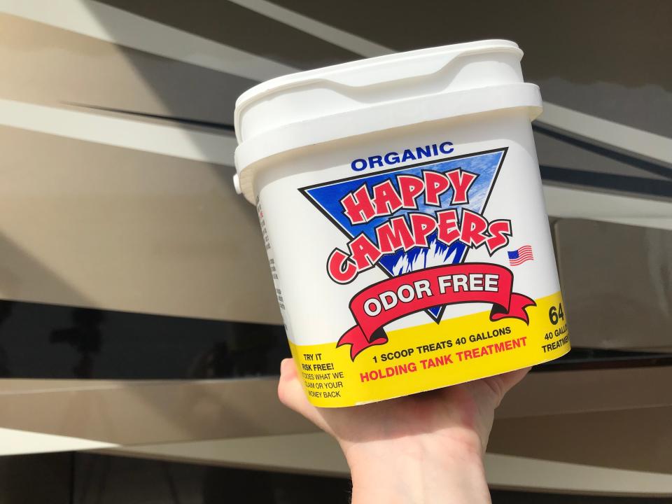 A hand holds the Happy Campers treatment container in front of the RV