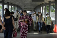 People wearing protective masks pass through a pedestrian bridge Friday, July 30, 2021, in Yokohama, south of Tokyo. Japan is set to expand the coronavirus state of emergency in Tokyo to neighboring prefectures including Saitama, Chiba and Kanagawa, where Yokohama is located, and the western city of Osaka as infections surge to new highs while the capital hosts the Olympics. (AP Photo/Kiichiro Sato)