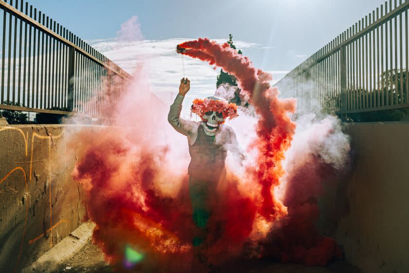 Downey, CA - August 11: Butch Locsin does one of his signature smoke performances in his handmade mask on a bridge over the L.A. River, on Thursday, Aug. 11, 2022 in Downey, CA. (Wesley Lapointe / Los Angeles Times)