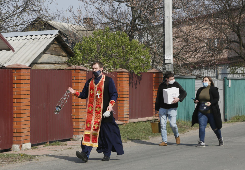 Priest of Ukrainian Orthodox Church Nazariy, wearing a face mask to protect against coronavirus, followed by his assistants, walks along the street to bless people on the Easter eve in the village of Nove close to capital Kyiv, Ukraine, Saturday, April, 18, 2020. All the Ukrainian churches have been closed for people because of COVID-19 outbreak, and believers wait for the priest right near their houses. For Orthodox Christians, this is normally a time of reflection, communal mourning and joyful release, of centuries-old ceremonies steeped in symbolism and tradition. But this year, Easter - by far the most significant religious holiday for the world's roughly 300 million Orthodox - has essentially been cancelled. (AP Photo/Efrem Lukatsky)