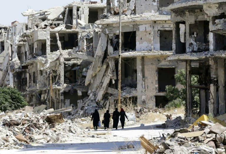 Women walk between destroyed buildings in the government-held Jouret al-Shiah neighbourhood of the central Syrian city of Homs