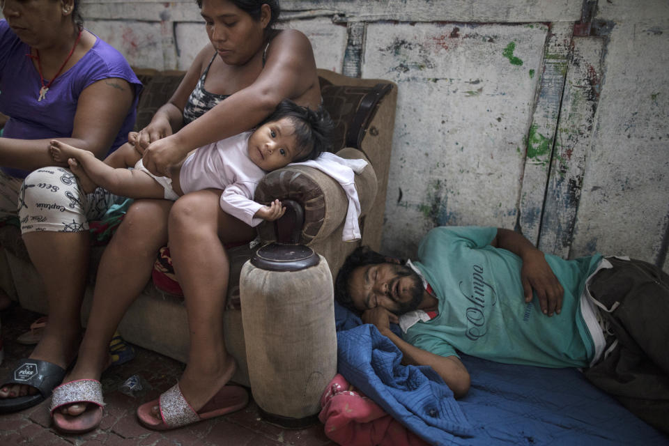 In this March 29, 2020 photo, Ivonne Garcia changes her daughter's diaper in her small room while her homeless cousin naps nearby, in the deteriorating building nicknamed "Luriganchito" after the country's most populous prison, in Lima, Peru. Because of the strict measures that include restricted public circulation taken by the government amid the new coronavirus pandemic, Garcia is allowing her homeless cousin to sleep in a corner of her room. (AP Photo/Rodrigo Abd)