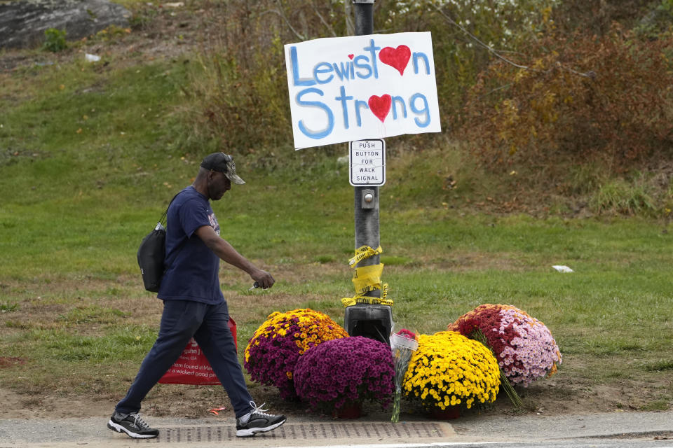 FILE - A man walks by flowers and a sign of support for the community, Oct. 28, 2023, in the wake of the mass shootings that occurred on Oct. 25, in Lewiston, Maine. A Maine law that can be used to restrict access to guns during a mental health crisis has been invoked more than a dozen times since the Oct. 25 mass shooting in Lewiston — the deadliest in state history — with several people invoking the name of the gunman who killed 18 people. (AP Photo/Robert F. Bukaty, File)