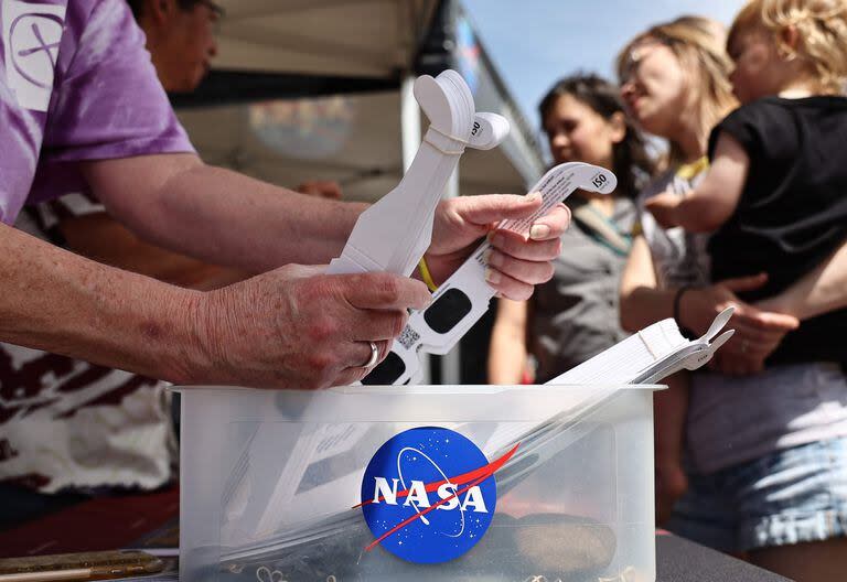 Una persona recoge gafas gratuitas para eclipses solares proporcionadas por la NASA en un stand de información de la NASA durante la celebración en la ciudad del eclipse solar del 8 de abril el 7 de abril de 2024 