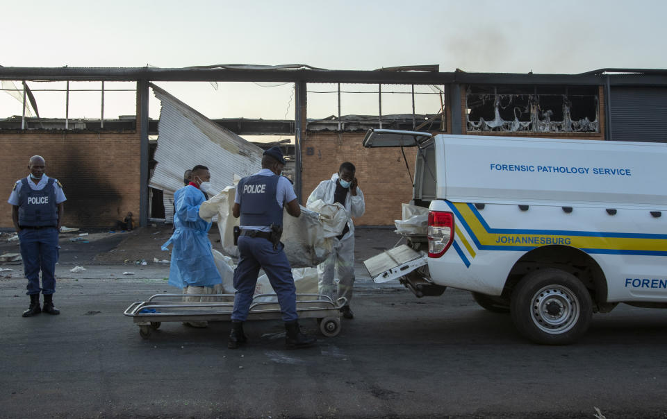 Police officers load bodies of two men that were found inside a burned shop in Johannesburg, South Africa, Sunday, July 11, 2021. Protests have spread from the KwaZulu Natal province to Johannesburg against the imprisonment of former South African President Jacob Zuma who was imprisoned last week for contempt of court. (AP Photo/Themba Hadebe)