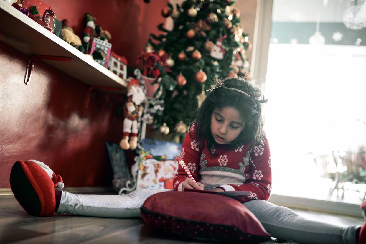 little girl writing her wishes on letter to santa under Christmas tree