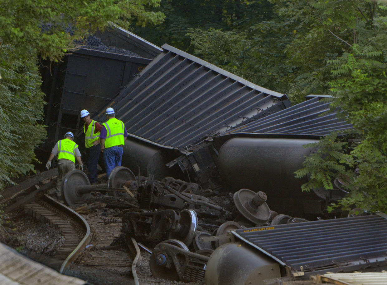 Three CSX employees in bright lime-green vests navigate debris and toppled hopper cars in 2012 at the scene of the derailment.