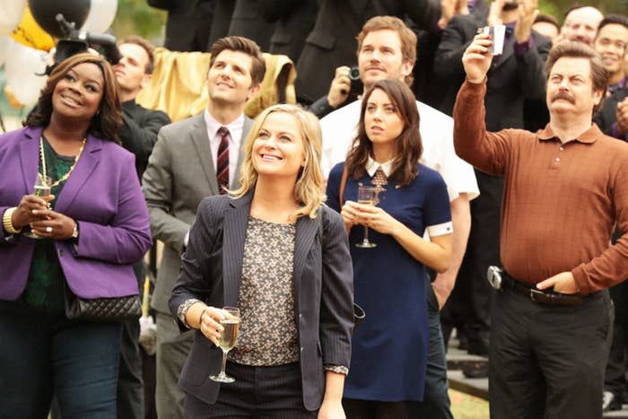 Cast of Parks and Rec looking up and smiling with champagne