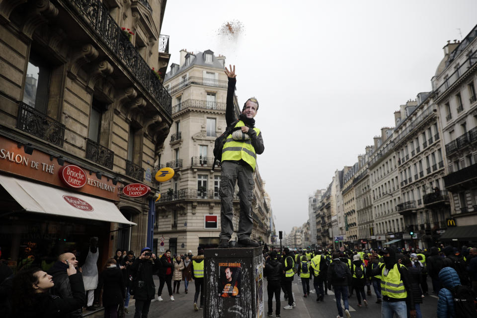 A yellow vest demonstrator wearing a mask of French President Emmanuel Macron throws breadcrumbs in the air during a march in Paris, Saturday, Jan.19, 2019. Hundreds of yellow vest protesters rallied in several French cities for a tenth consecutive weekend on Saturday despite a national debate launched this week by President Emmanuel Macron aimed at assuaging their anger(AP Photo/Kamil Zihnioglu)