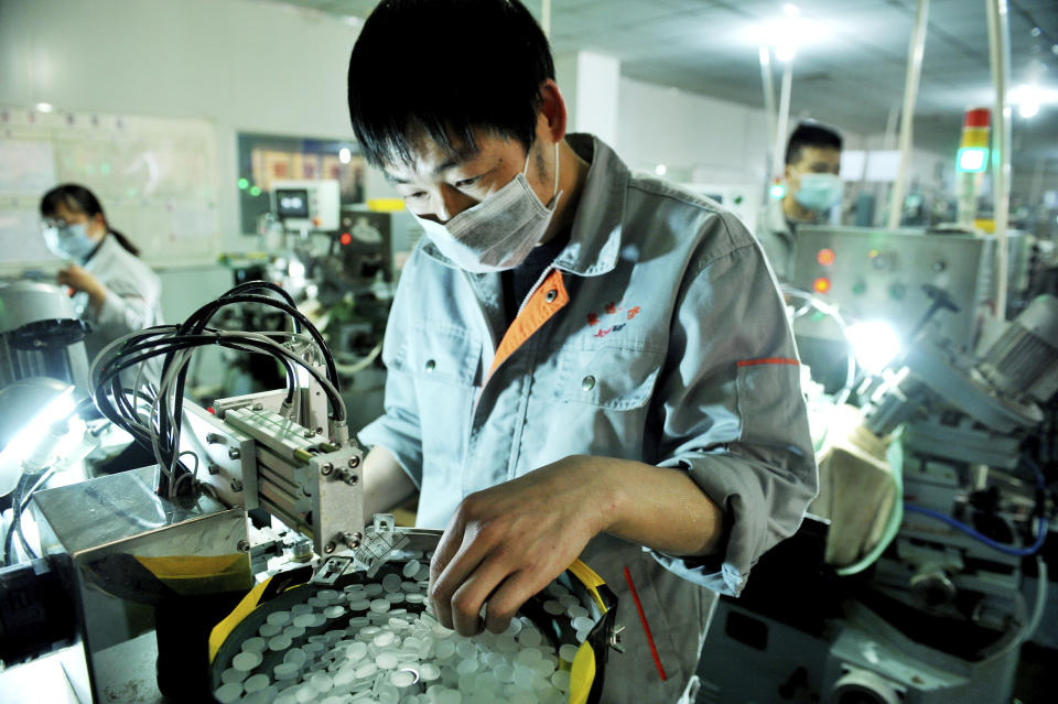 In this photo taken Feb. 23, 2020, workers make optical lenses in a factory in Dexing city in central China's Jiangxi province. Factories that make the world's smartphones, toys and other goods are struggling to reopen after a virus outbreak idled China's economy. But even with the ruling Communist Party promising help, companies and economists say it may be months before production is back to normal. (Chinatopix Via AP)