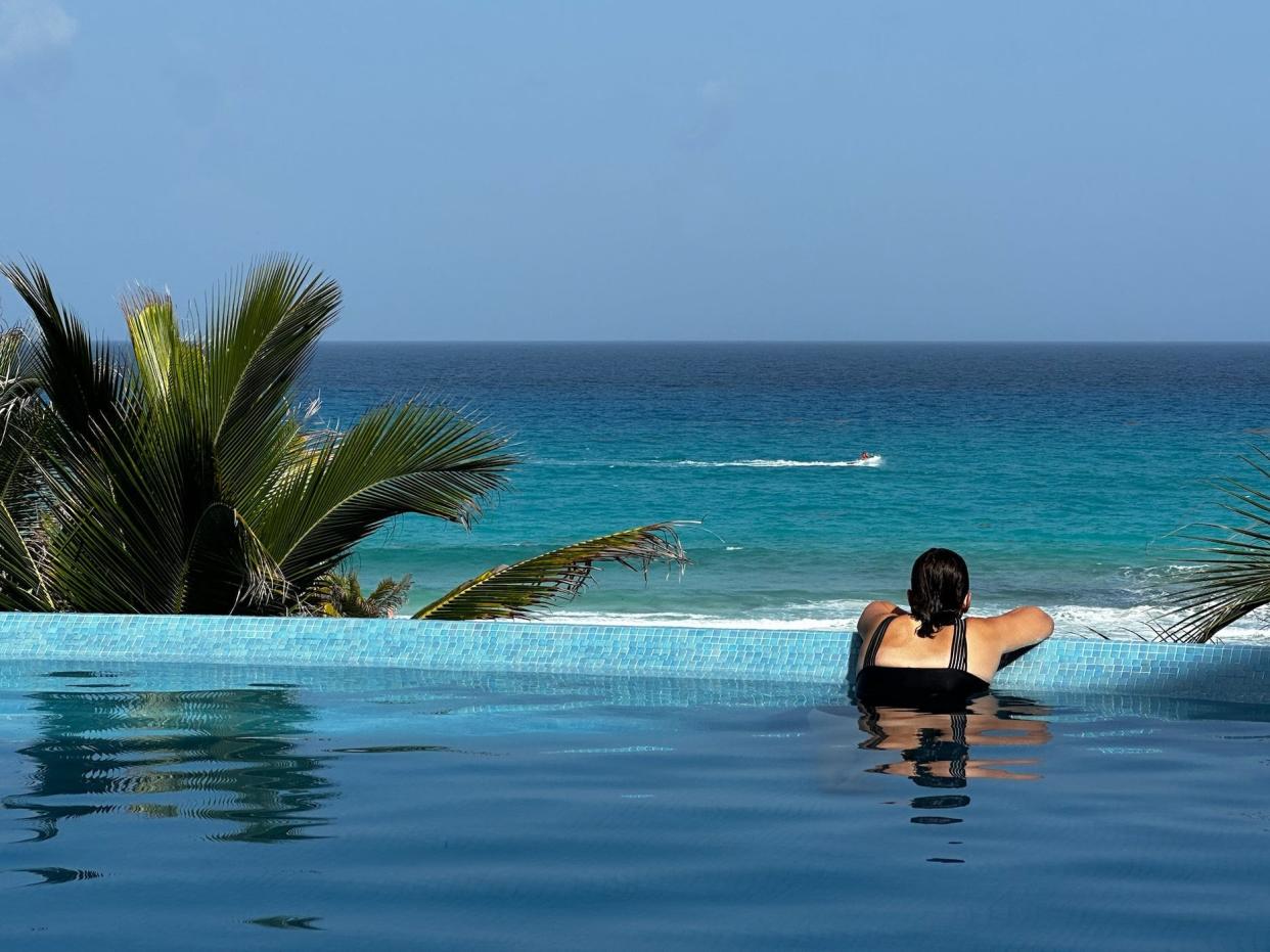 back of a woman leaning against the ledge of a nice pool overlook the ocean