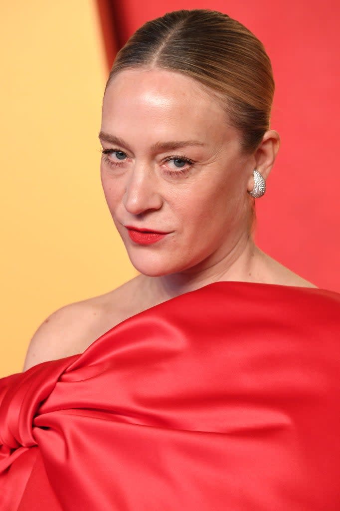 Woman in elegant red off-the-shoulder gown and large earrings, looking over shoulder