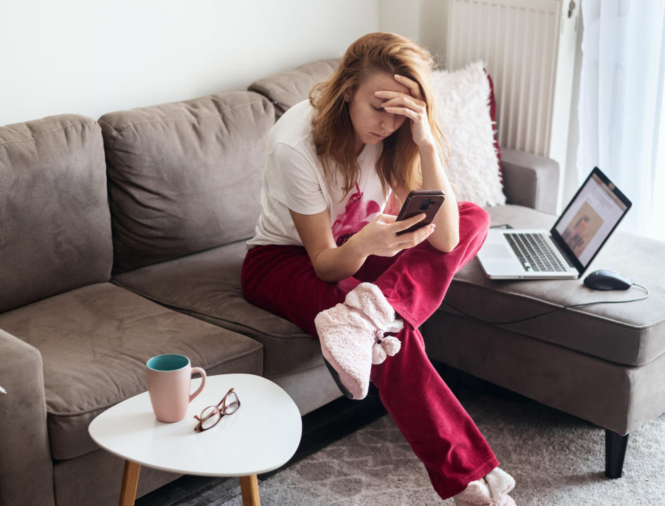 A young woman in red pants looks anxiously at her phone