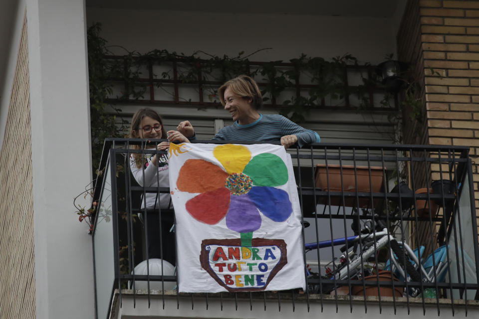 In this photo taken on Friday, March 13, 2020, 8-year hold Flavia is flanked by her mother Silvia as they place a banner reading "Everything will be alright" on the balcony of their apartment in Rome. The nationwide lockdown to slow coronavirus is still early days for much of Italy, but Italians are already are showing signs of solidarity. This week, children’s drawings of rainbows are appearing all over social media as well as on balconies and windows in major cities ready, ‘’Andra’ tutto bene,’’ Italian for ‘’Everything will be alright.’’ For most people, the new coronavirus causes only mild or moderate symptoms. For some, it can cause more severe illness, especially in older adults and people with existing health problems. (AP Photo/Alessandra Tarantino)