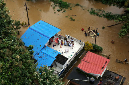 People wait for aid on the roof of their house at a flooded area in Kerala, August 17, 2018. REUTERS/Sivaram V