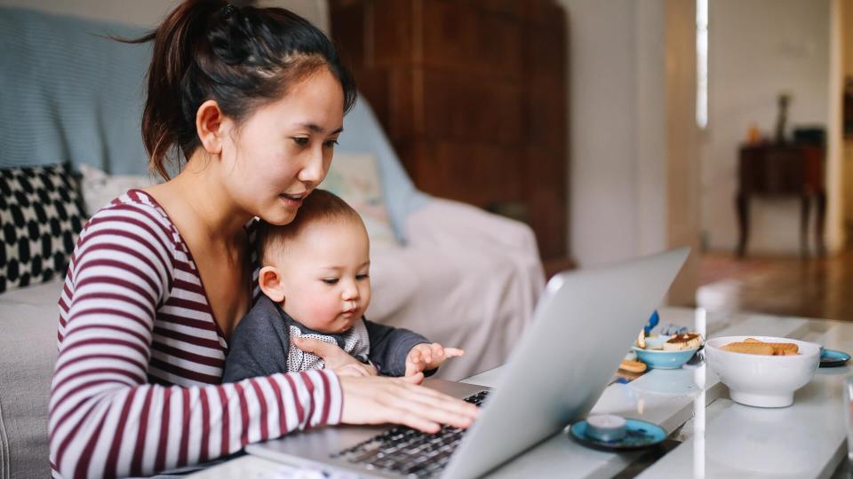 Portrait of a young Asian woman sitting at home, doing some freelance job while taking care of her little baby boy.