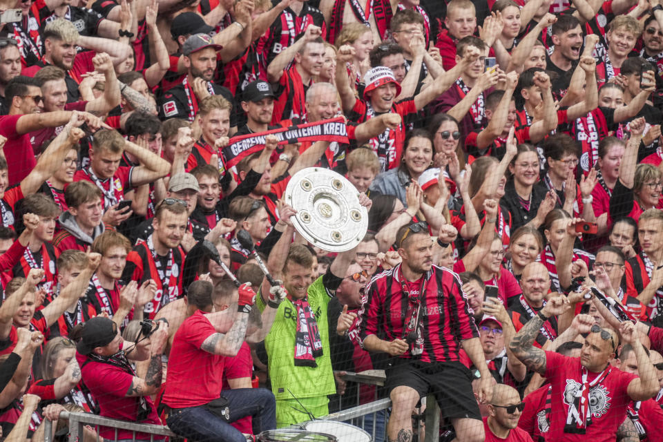 FILE - Leverkusen's goalkeeper Lukas Hradecky celebrates with fans holding the trophy as his team won the German Bundesliga, after the German Bundesliga soccer match between Bayer Leverkusen and FC Augsburg at the BayArena in Leverkusen, Germany, Saturday, May 18, 2024. A low-rise city of 167,000 that grew up around the factories of the pharmaceuticals giant Bayer, Leverkusen has little to draw tourists besides its internationally famed soccer club. The team finished an entire German Bundesliga season unbeaten Saturday and is now targeting trophies in the Europa League and German Cup. (AP Photo/Michael Probst, File)