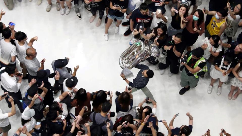 香港新界沙田新城市廣場購物商場內一位示威者舉著低音號走過其他示威者（11/9/2019）
