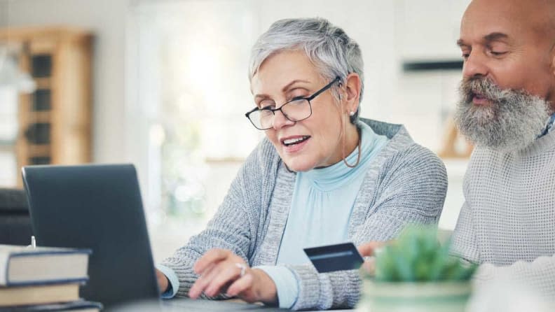 Two elderly people shopping on a laptop with a credit card.