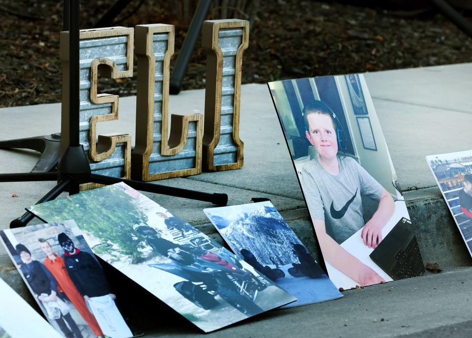 Photos and and a sign of Eli Mitchell’s name sit on the sidewalk and gutter as a large group of people gather on Wednesday, April 26, 2023, in West Jordan at 9000 South and 1510 West where 13-year-old Eli Mitchell was killed by a drunk driver one year ago. | Scott G Winterton, Deseret News