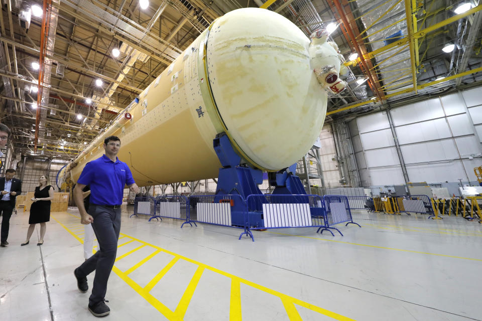 People walk in front of the core stage of the Space Launch System, which will power the Artemis 1 lunar mission, as NASA Administrator Jim Bridenstinein tours the NASA Michaud Assembly Facility in New Orleans, Thursday, Aug. 15, 2019. (AP Photo/Gerald Herbert)