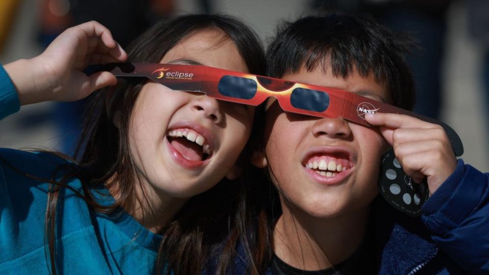 Miriam Toy (L) and Oliver Toy share a pair of eclipse glasses that Nasa was handing out as they await the eclipse on April 08, 2024, in Houlton, Maine.