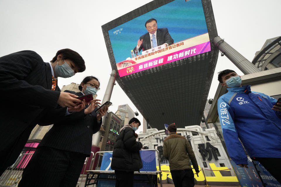 People walk past a large video screen at a shopping mall showing Chinese Premier Li Keqiang as he speaks during a press conference after the closing session of China's National People's Congress (NPC) in Beijing, Friday, March 11, 2022. (AP Photo/Ng Han Guan)