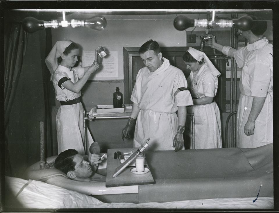 A patient in a saline bath, whilst staff work in the background, at the Queen Victoria Hospital, Holtye Road, East Grinstead, West Sussex