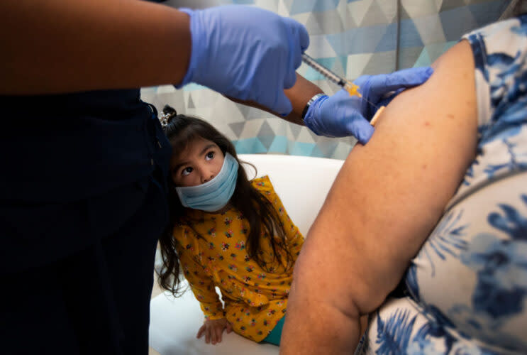 Small child looks up at her grandparent getting a vaccine, needle in foreground