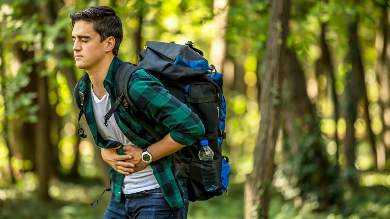  Man holding stomach in discomfort while hiking. 