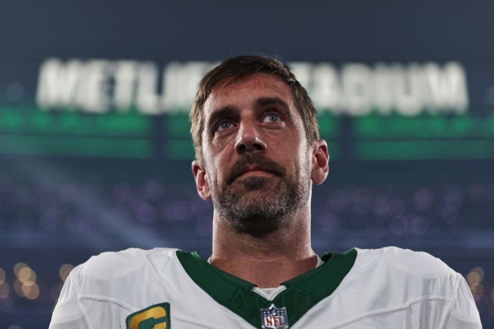 aaron rodgers looking toward the sky while stnading in his jets uniform