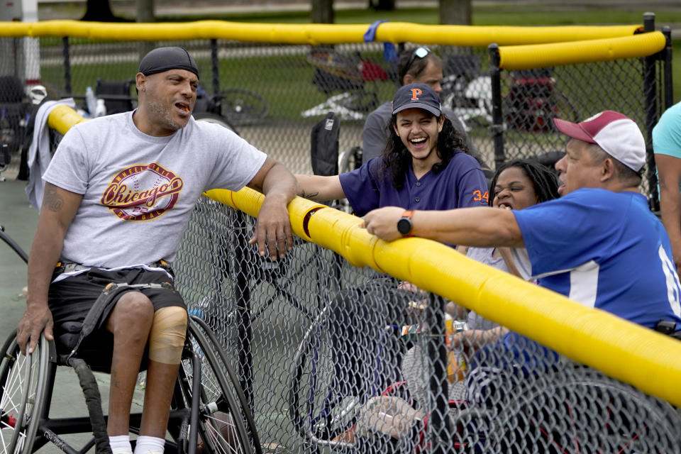 Jonathan Annicks, second from left, shares a laugh with teammates on an adult handicap softball team Saturday, June 11, 2022, in Chicago. With more time, post-graduation, Annicks returned to the softball field, a concrete diamond on Chicago's North Side where adults and children with various disabilities play the no-glove version of the game in wheelchairs with a slightly larger ball. (AP Photo/Charles Rex Arbogast)