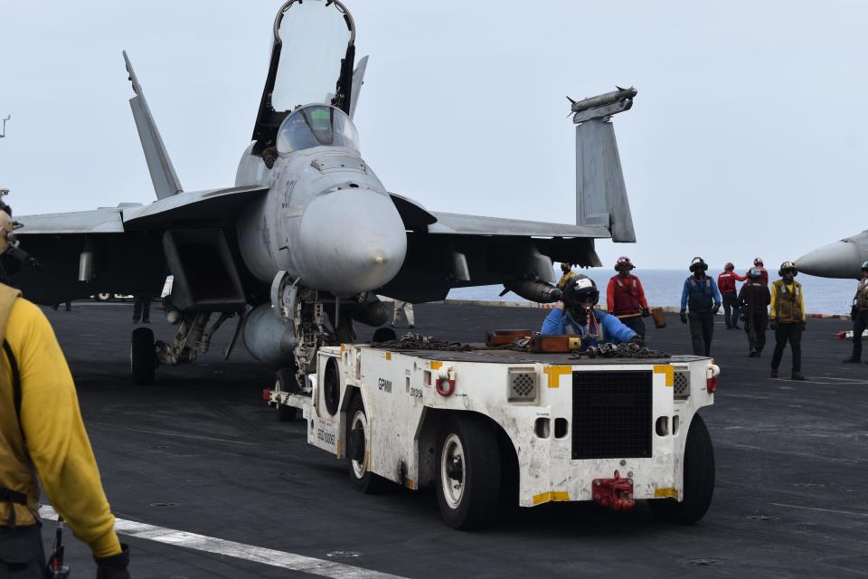 A fighter jet is towed across the flight deck of the USS Dwight D. Eisenhower.