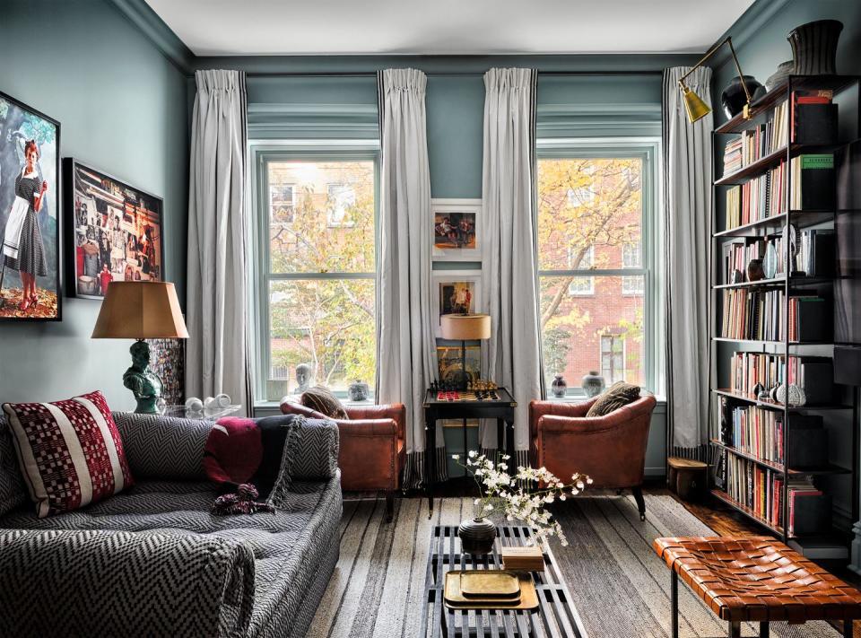 family room with tall curtained windows in the background with a small table with deep comfy chairs pulled up to it and shelving full of books to the right and a black and white zigzag pattern sofa opposite and a