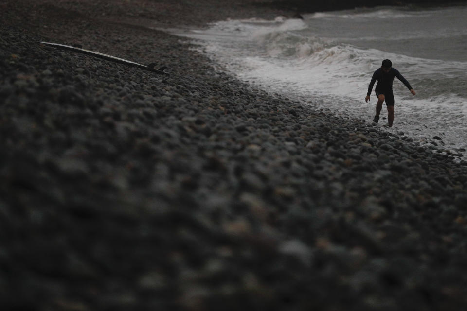 A surfer picks his way across rocks as he leaves the water at Makaha beach in Lima, Peru, as darkness falls Thursday, July 25, 2019. Today, dozens of schools teach tourists from across the world how to ride waves at beaches with Hawaiian names in Lima's Miraflores district, while professional surfers from across the Americas prepare to compete when the sport is featured for the first time in the Pan American Games in the Peruvian capital.(AP Photo/Rebecca Blackwell)