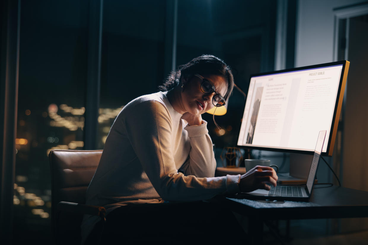 Exhausted business woman working late at her dimly lit office desk to meet a project deadline