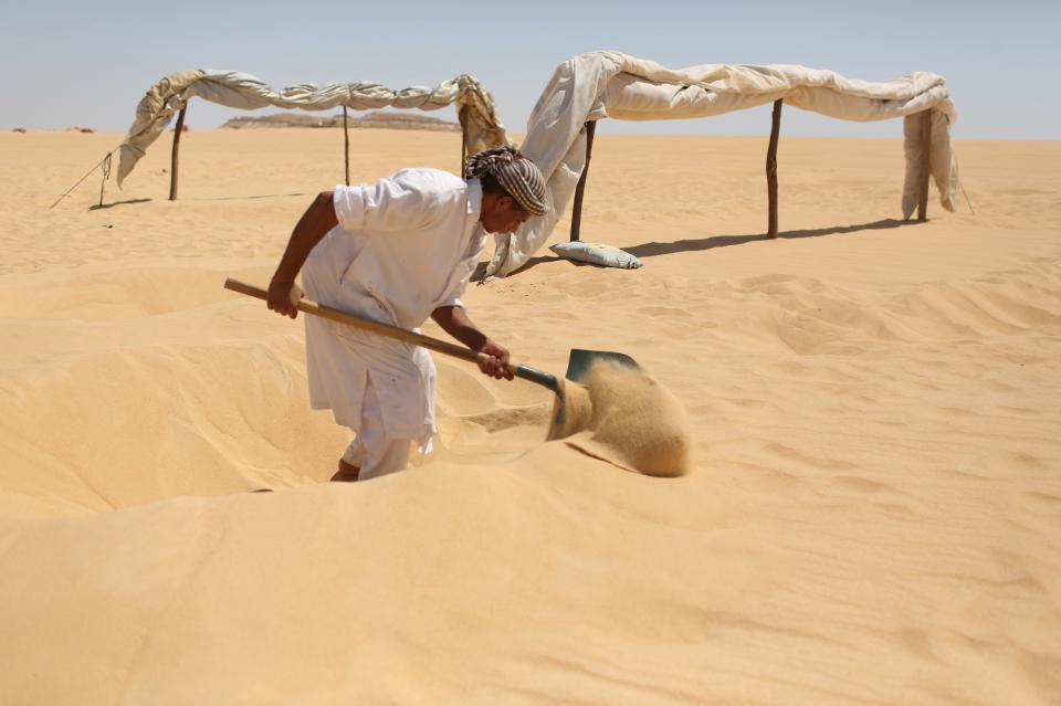 A worker digs fresh holes in the sand in front of small tents for patients who will take sand baths in Siwa, Egypt, August 12, 2015. (REUTERS/Asmaa Waguih)