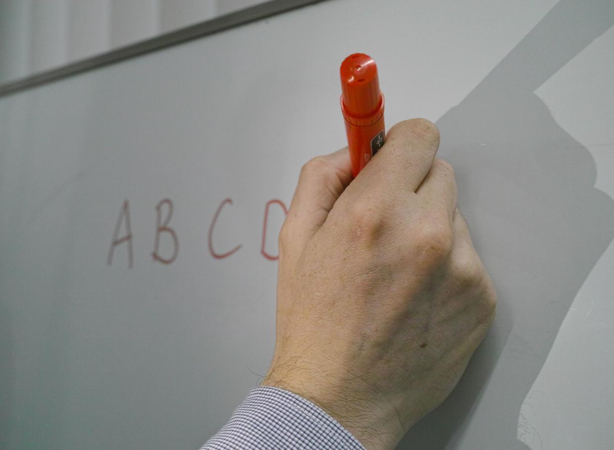 A male teacher's hand writing the alphabet on the board