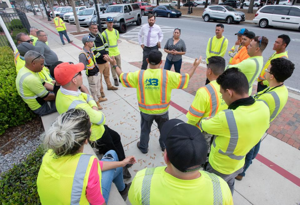 A crew of tree trimmers consult with attorney Josef Mitkevicius, top center, while demonstrating in front of the Federal Courthouse in downtown Pensacola on Tuesday, Feb. 28, 2023.  The crew of approximately two dozen workers hired by Buford's Construction, subcontracted by FPL to do tree trimming, were allegedly fired for not speaking English.