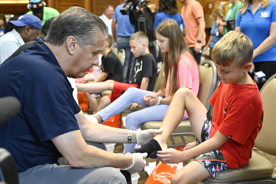 University of Kentucky men's head basketball coach John Calipari, left, puts socks on one of the kids whose families have been displaced from the eastern Kentucky flooding at a shoe giveaway for flood victims at Jenny Wiley State Park in Prestonsburg, Ky., Tuesday, Aug. 23, 2022. (AP Photo/Timothy D. Easley)