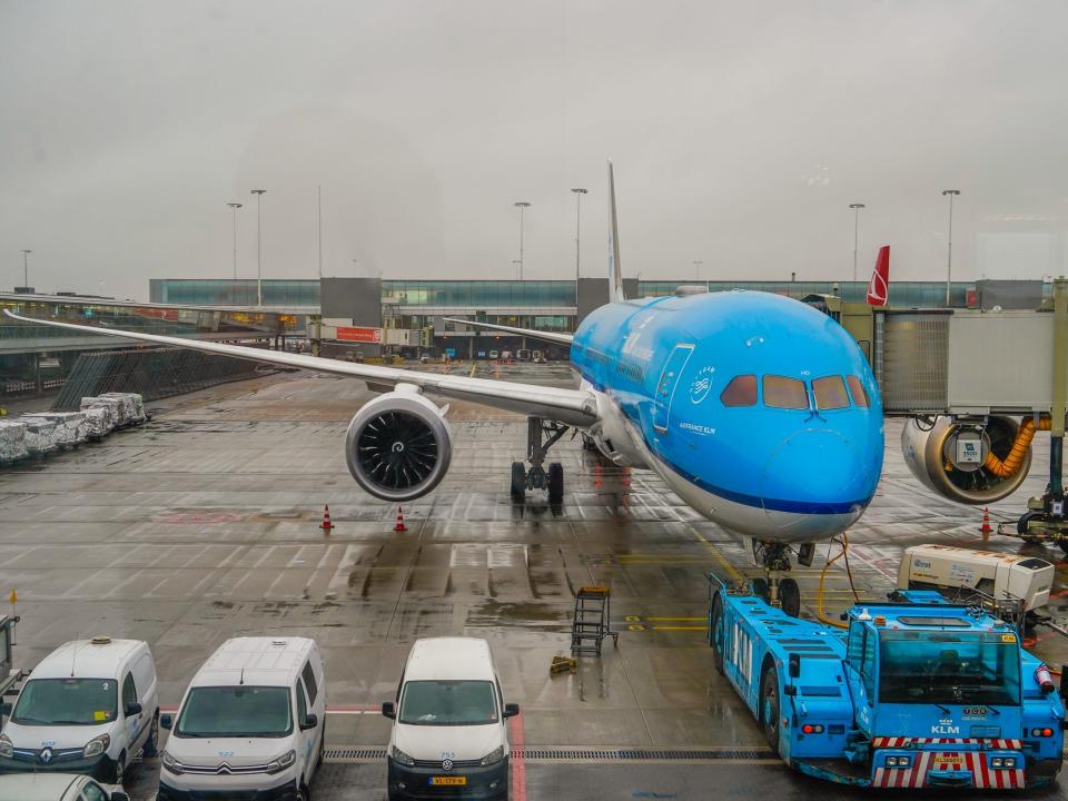 A blue and white plane parked at a gate on a rainy day