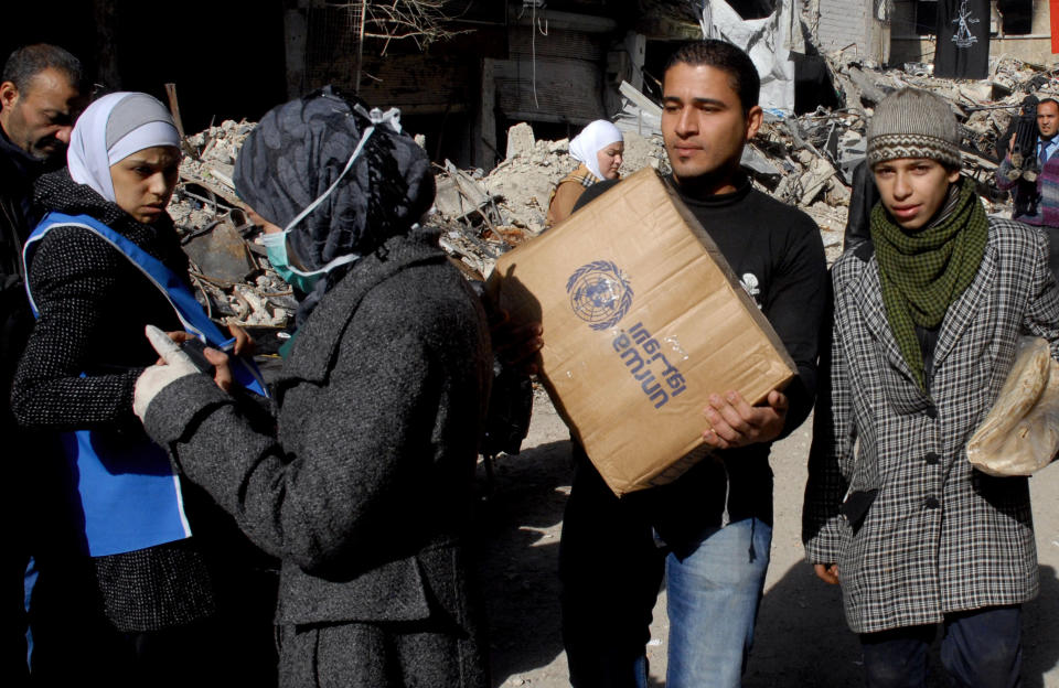 In this photo released by the Syrian official news agency SANA, Palestinian residents of the besieged refugee camp of Yarmouk carries supplies given to them by the United Nations at the gate of the camp on the southern edge of the Syrian capital Damascus, Syria, Thursday, Jan. 30, 2014. The U.N. says 600 food parcels were distributed in the camp where activists say at least 85 people have died as a result of lack of food and medicine since mid-2013. (AP Photo/SANA)