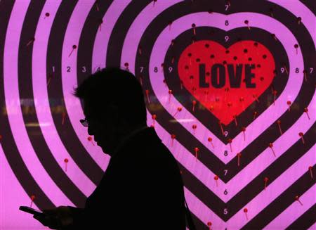 A man using his mobile phone walks past a shop window with signs advertising the upcoming Valentine's Day, at a luxury store in Tokyo January 30, 2014. REUTERS/Yuya Shino